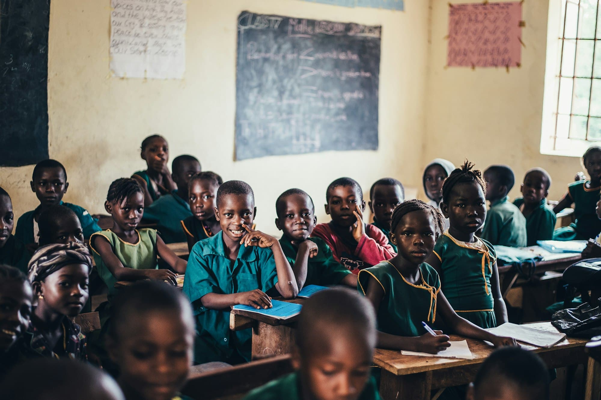 Primary school pupils in green uniforms smiling at their desks